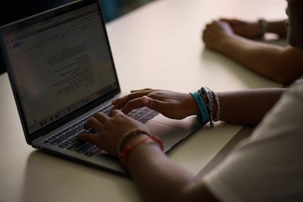 A close up of a student’s hands working on a laptop at a desk.